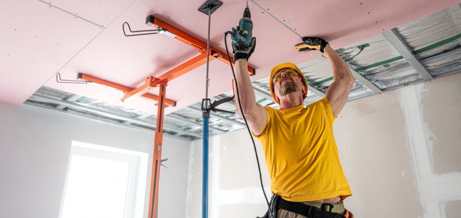 The,worker,screwing,plasterboard,to,the,ceiling.,he,is,using